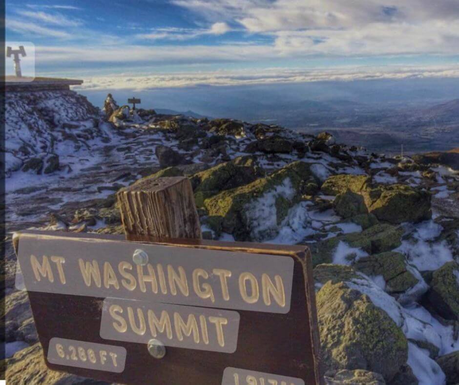 A sign reading Mt Washington Summit 6288 feet overlooking New Hampshire fronm the top of Mount Washington